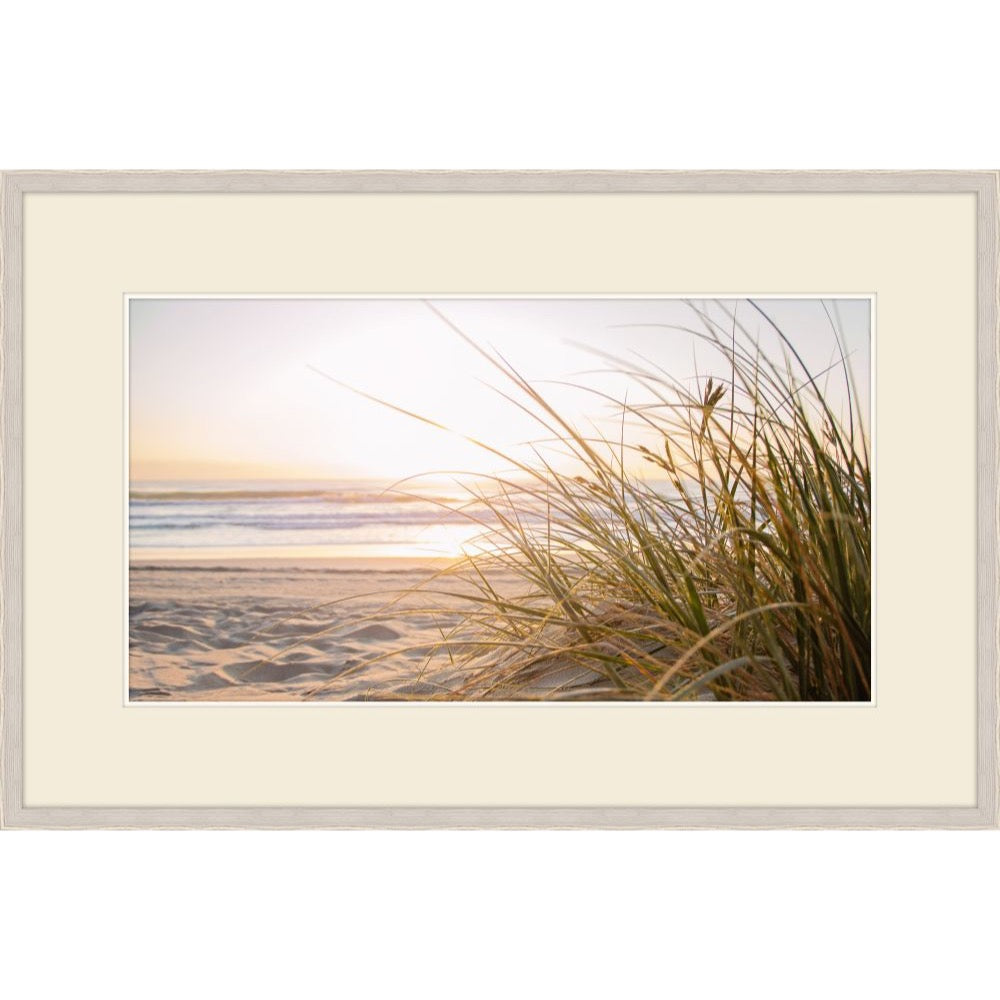 Photograph of dune grass backlit by a warm sunrise over the shoreline