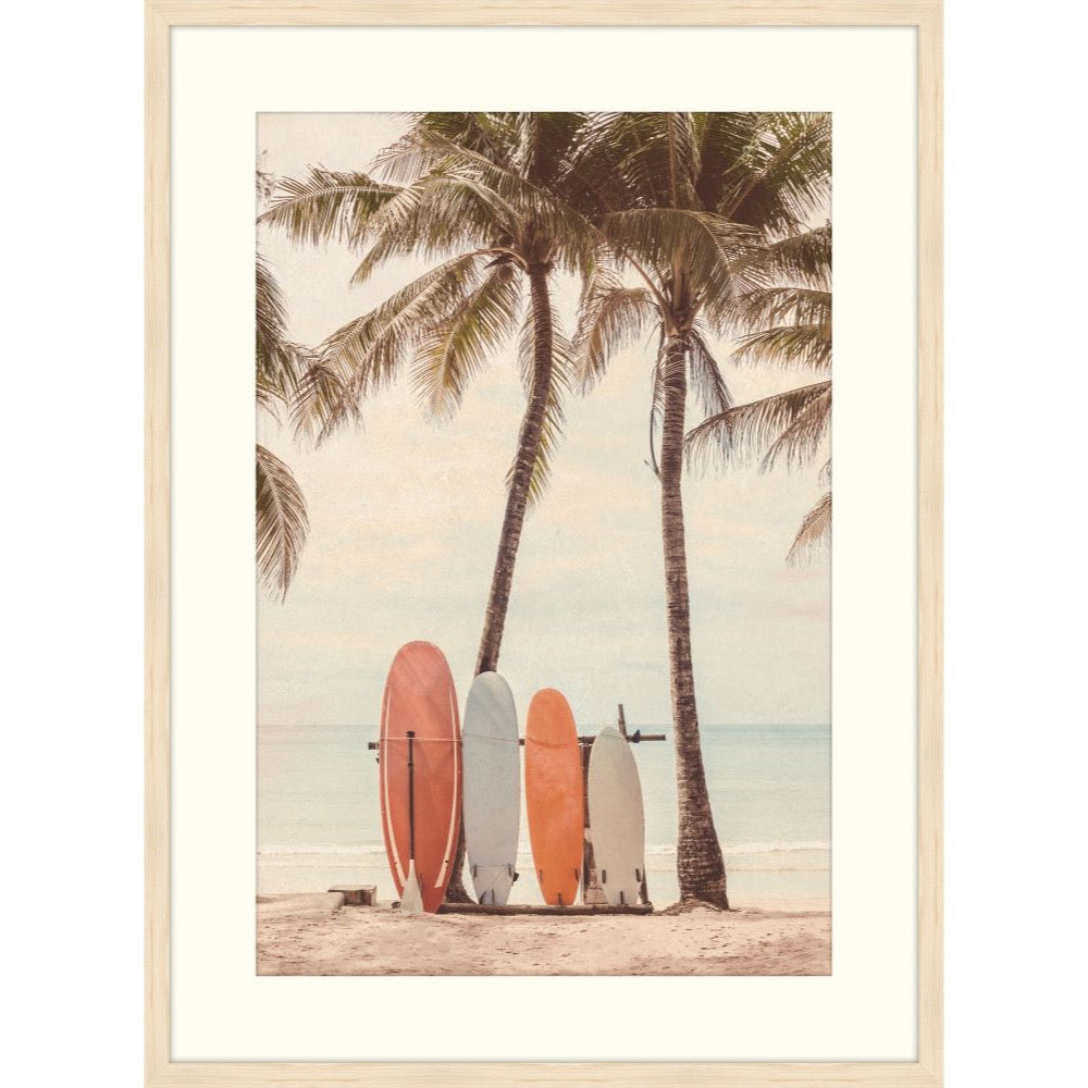 Warm-toned photograph of coral and cream surfboards between two palm trees on a beach