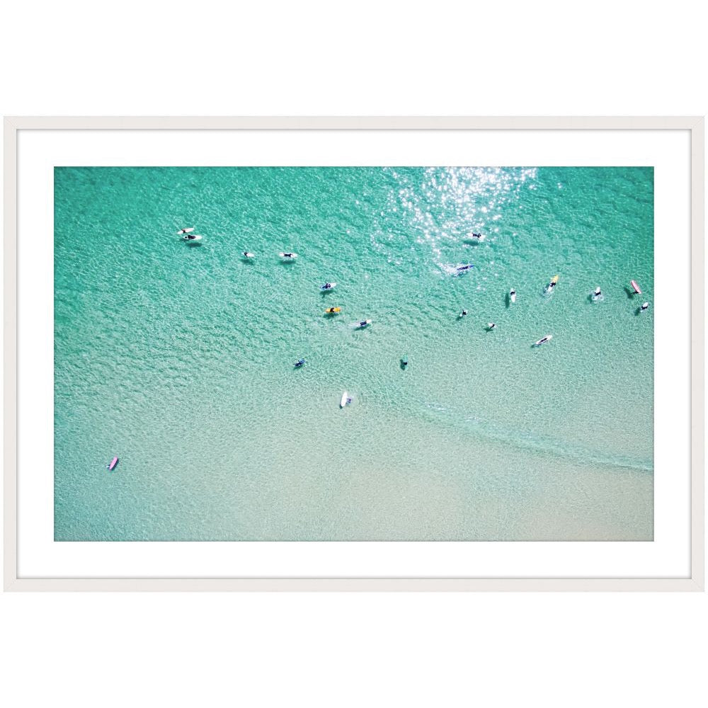 Aerial photograph of surfers in clear turquoise water over pale sand