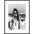 Black and white photograph of a woman in sunglasses and an oversized straw hat by the sea