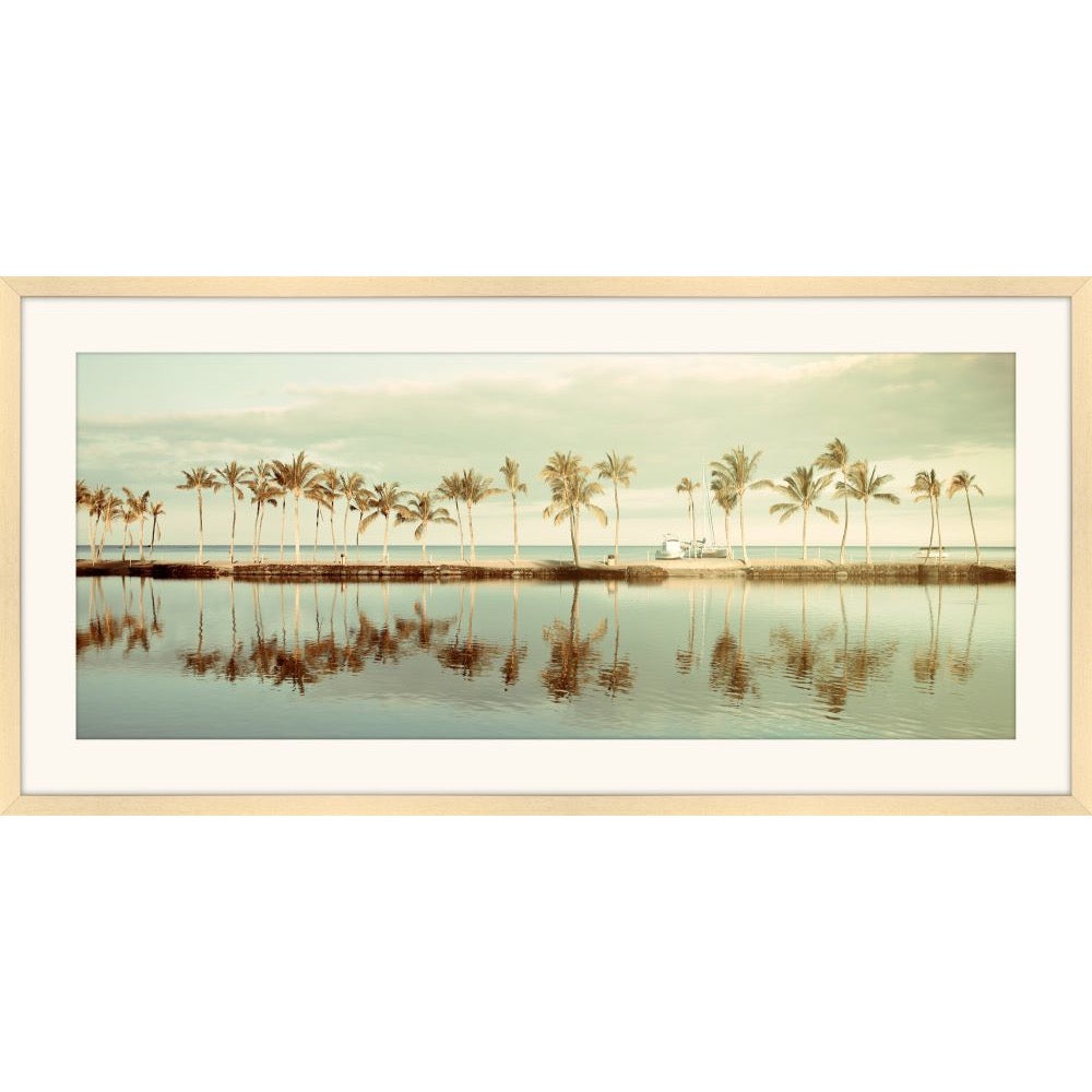 Panoramic photograph of palm trees reflected in a still inlet at dawn in soft green and gold