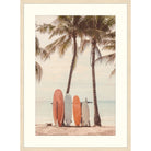 Warm-toned photograph of coral and cream surfboards between two palm trees on a beach
