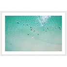 Aerial photograph of surfers in clear turquoise water over pale sand