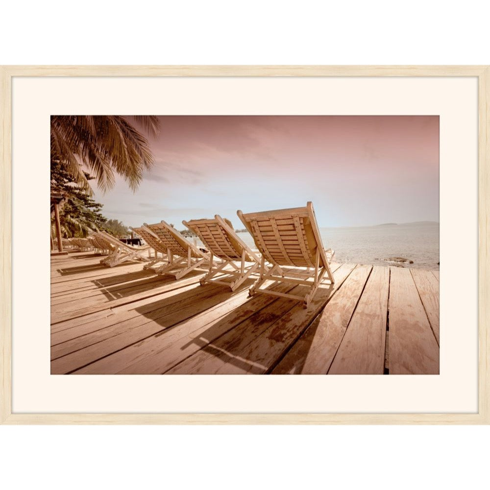 Rose-tinted photograph of wooden lounge chairs on a deck facing the ocean