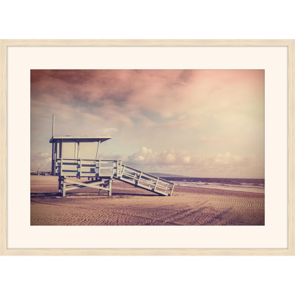 Pink-toned photograph of a lifeguard stand on an empty beach at sunset